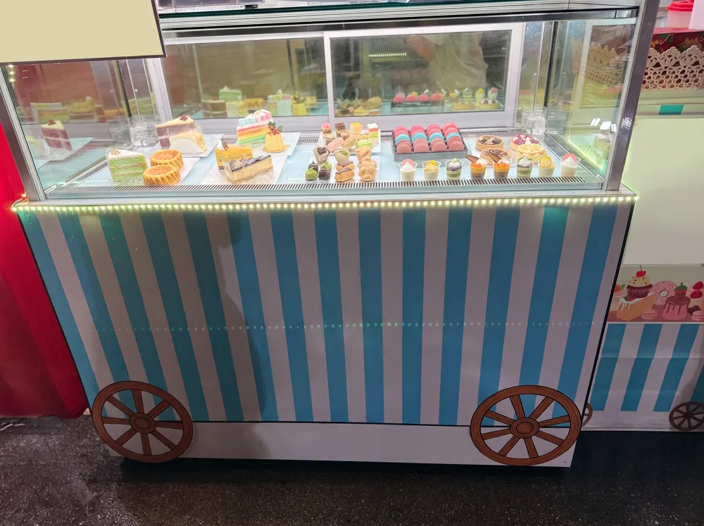 AANRS cake chiller rental Singapore, long glass cake display dressed as a striped fairground cart and filled with cakes and macarons