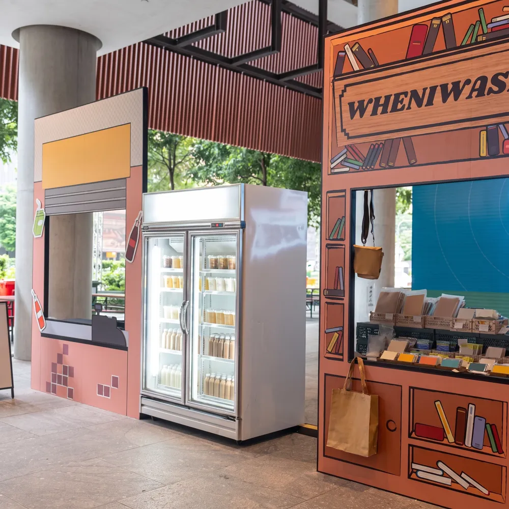 AANRS drink chiller rental Singapore, two-door chiller stocked with bottled drinks between illustrated set pieces at an outdoor pop-up
