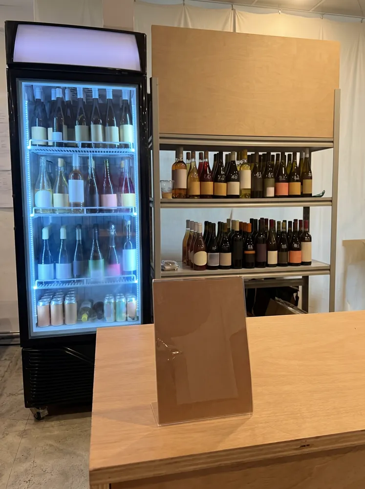 AANRS drink chiller rental Singapore, upright glass-door chiller filled with wine bottles beside open wine shelving under a marquee