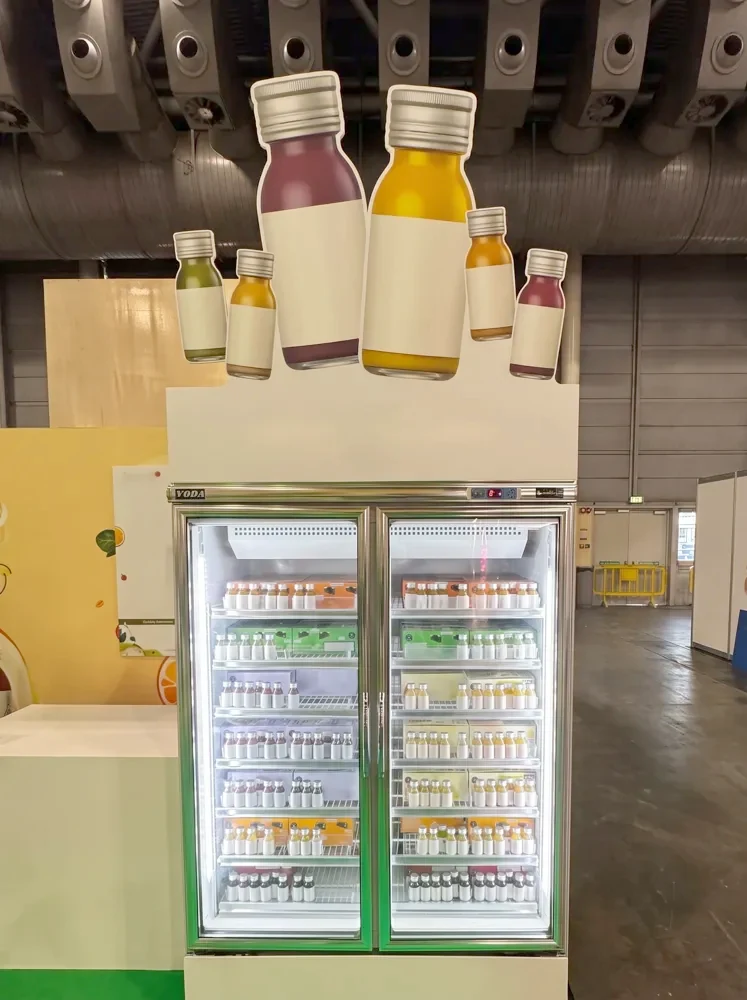 Juice chiller under a giant bottle display at an expo